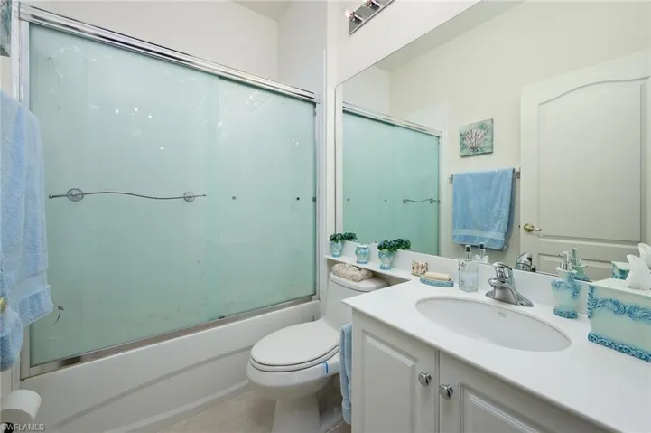 Full bathroom with tile floors, bath / shower combo with glass door, toilet, and vanity with extensive cabinet space