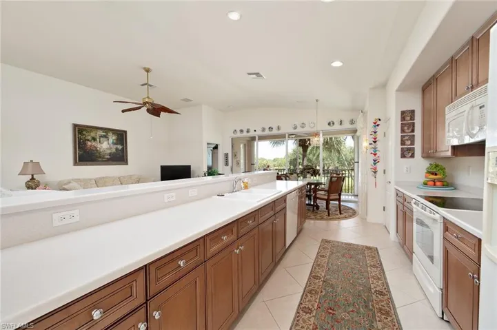 Kitchen with ceiling fan, white appliances, light tile flooring, sink, and lofted ceiling