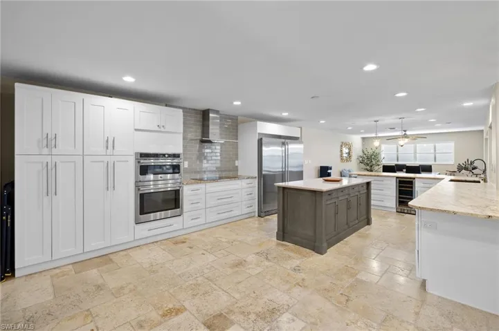 Kitchen featuring white cabinets, wall chimney range hood, beverage cooler, backsplash, and appliances with stainless steel finishes