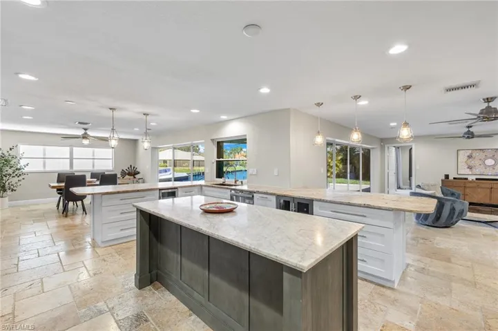 Kitchen with light stone countertops, a spacious island, hanging light fixtures, ceiling fan, and dishwasher