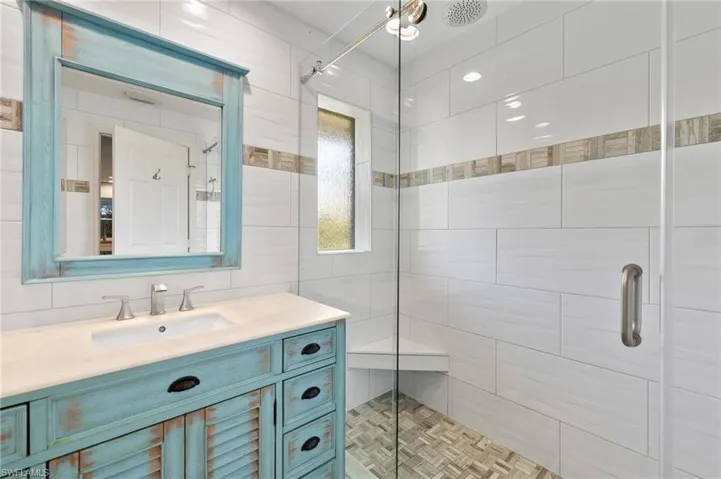 Bathroom featuring a shower with shower door, vanity, parquet floors, and tile walls