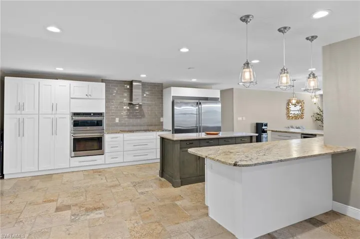 Kitchen with tasteful backsplash, a center island, wall chimney exhaust hood, white cabinets, and appliances with stainless steel finishes