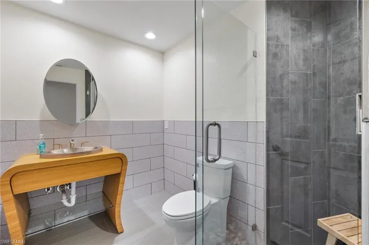 Bathroom featuring tile flooring, walk in shower, tile walls, and toilet