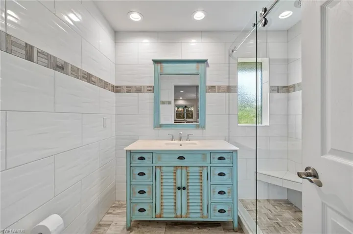 Bathroom featuring tile walls, walk in shower, wood-type flooring, and vanity