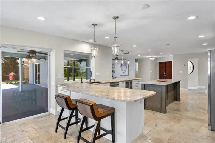 Kitchen with decorative light fixtures, sink, light stone countertops, and ceiling fan