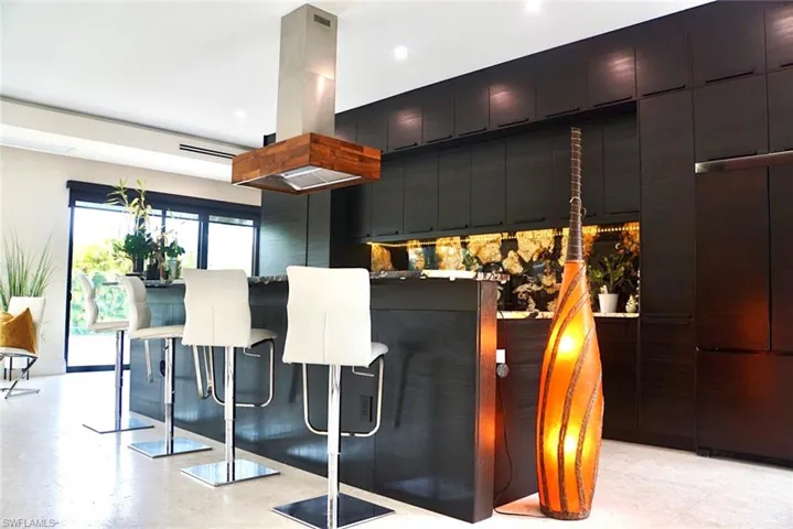 Kitchen with a kitchen breakfast bar, built in refrigerator, island range hood, and backsplash