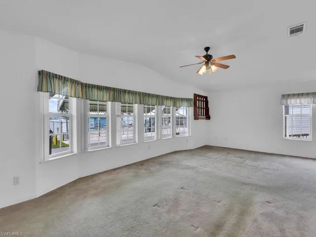 Carpeted empty room featuring ceiling fan and vaulted ceiling
