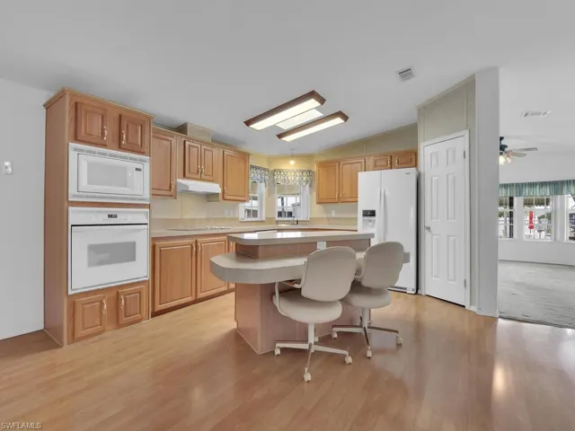 Kitchen featuring white appliances, a center island, lofted ceiling, and light hardwood / wood-style floors