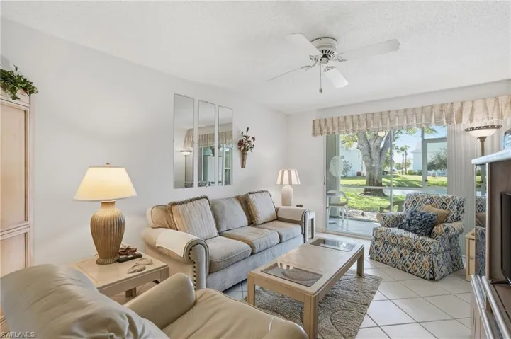 Living room with a ceiling fan, light tile patterned flooring, and a textured ceiling