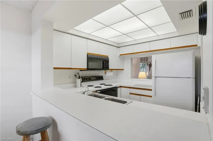 Two tone kitchen featuring light countertops, white appliances, a peninsula, and two tone color scheme