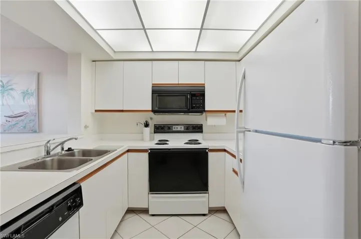Kitchen with freestanding refrigerator, electric range, white cabinetry, light countertops, and black microwave