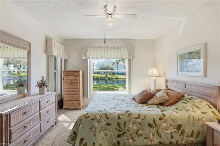 Bedroom with light carpet, a ceiling fan, a water view, and a textured ceiling