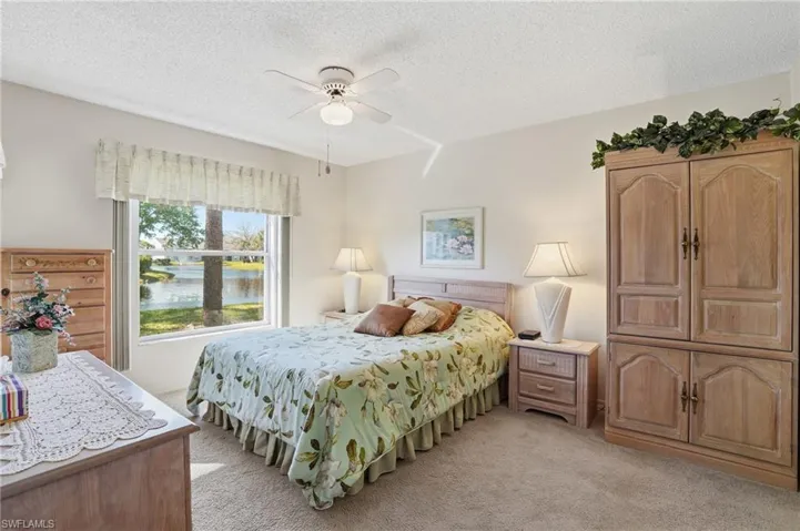 Bedroom featuring a textured ceiling, light colored carpet, a ceiling fan, and a water view