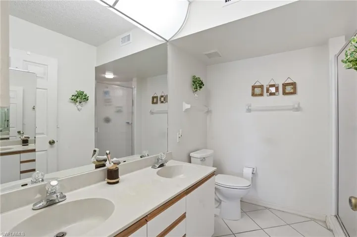 Bathroom featuring double vanity, a stall shower, light tile patterned floors, and a textured ceiling