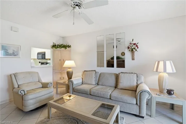 Living room with ceiling fan, light tile patterned floors, and a textured ceiling