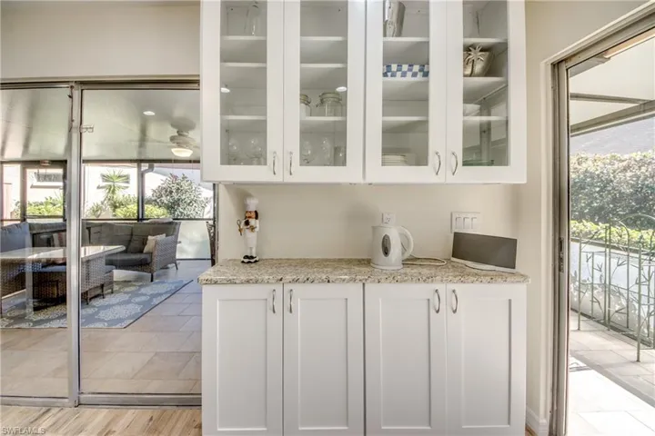 Bar featuring white cabinets, light stone counters, and glass fronted cabinets