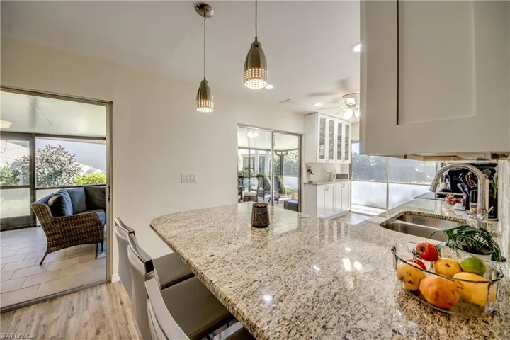 Kitchen featuring light stone counters, hanging light fixtures, a peninsula, white cabinets, and glass insert cabinets