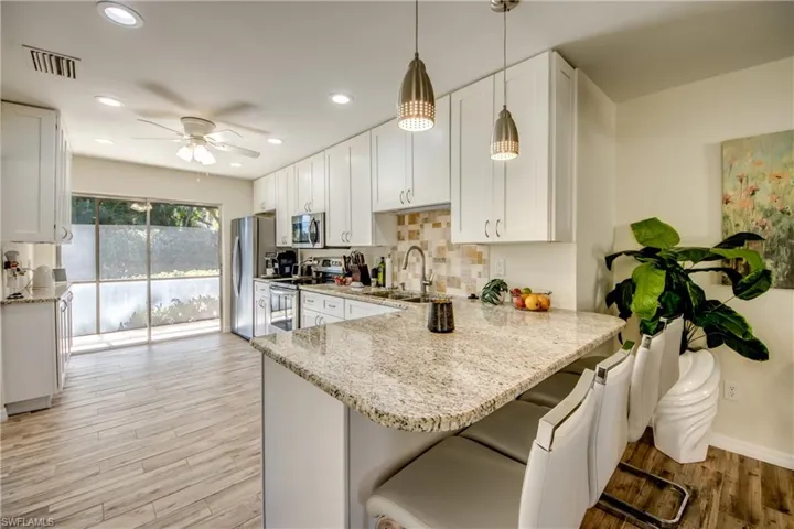 Kitchen featuring a peninsula, light wood-type flooring, light stone counters, and white cabinetry
