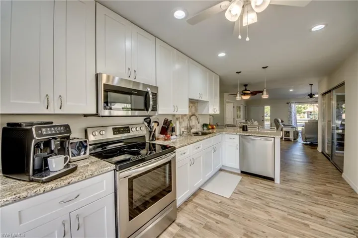 Kitchen featuring stainless steel appliances, white cabinets, light stone counters, hanging light fixtures, and a peninsula