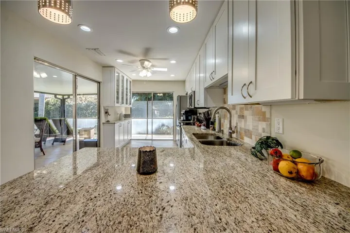 Kitchen featuring white cabinetry, light stone countertops, glass insert cabinets, decorative backsplash, and a ceiling fan