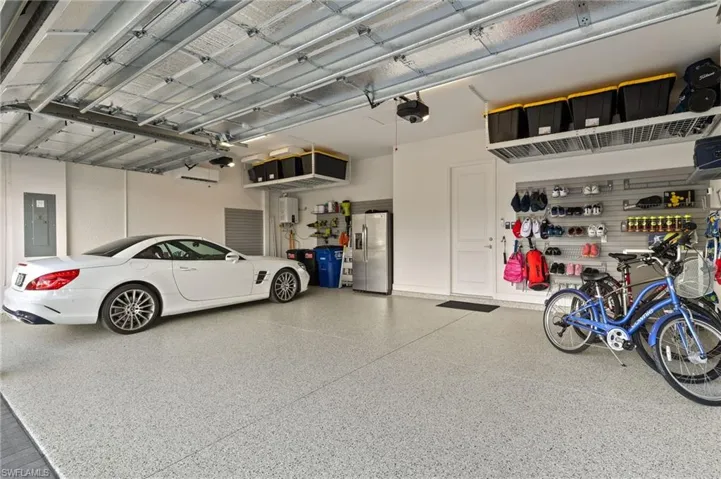 Garage with electric panel, stainless steel refrigerator with ice dispenser, and a garage door opener