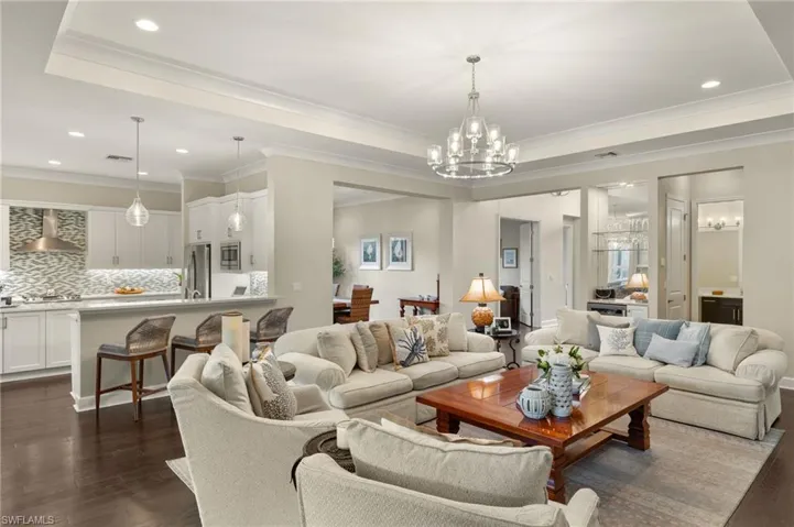 Living room with ornamental molding, a raised ceiling, dark hardwood / wood-style floors, and a chandelier