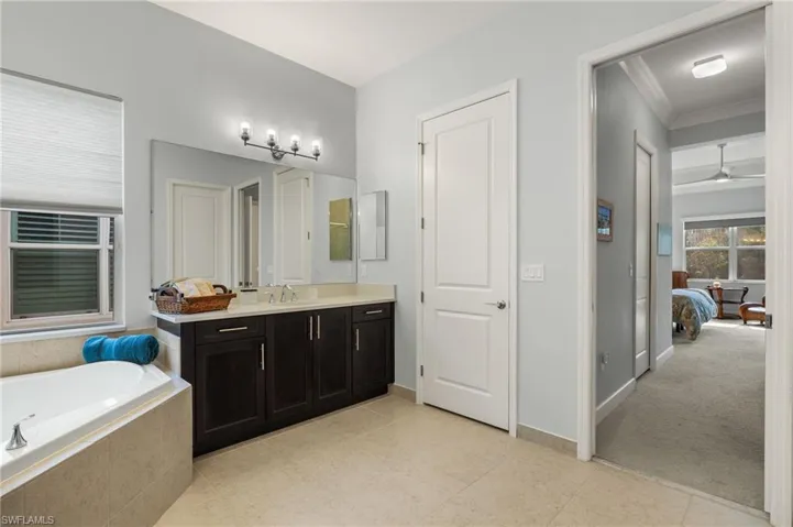 Bathroom featuring tiled tub, vanity, ceiling fan, and crown molding