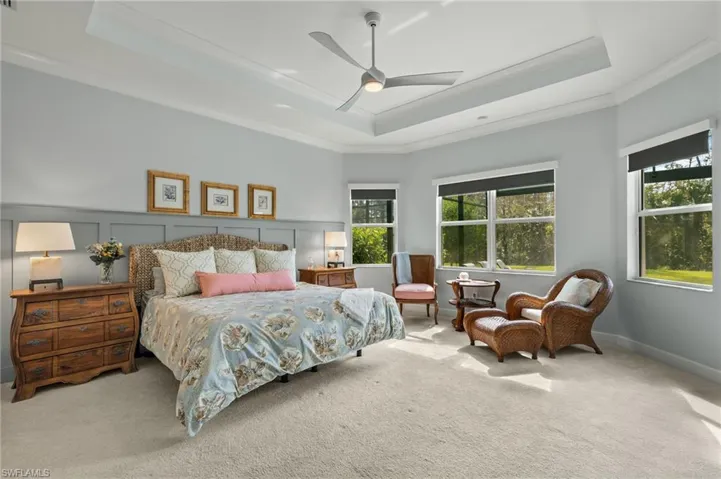 Bedroom with light carpet, multiple windows, ceiling fan, and a tray ceiling