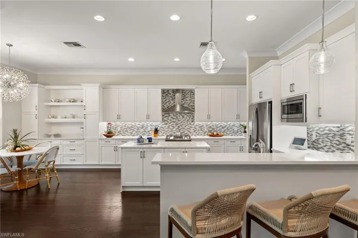 Kitchen featuring stainless steel appliances, dark hardwood / wood-style flooring, white cabinets, hanging light fixtures, and wall chimney range hood