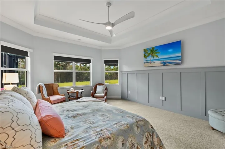 Carpeted bedroom featuring ornamental molding, ceiling fan, and a raised ceiling