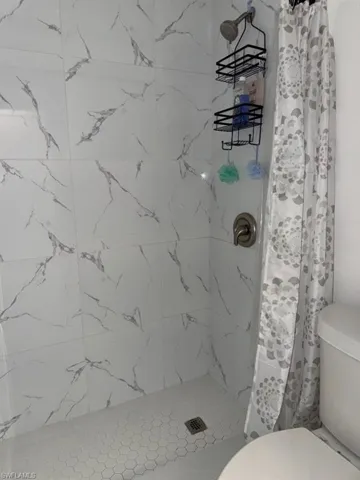 Shower enclosure featuring large format white tile walls with gray veining and a hexagonal mosaic tile floor