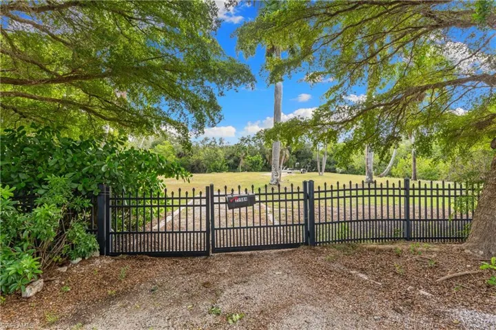 Black metal gate with a gravel drive, expansive grassy area, and mature trees
