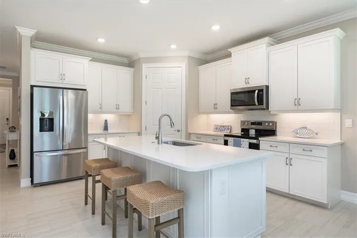Kitchen with stainless steel appliances, light countertops, a center island with sink, tasteful backsplash, and a kitchen bar
