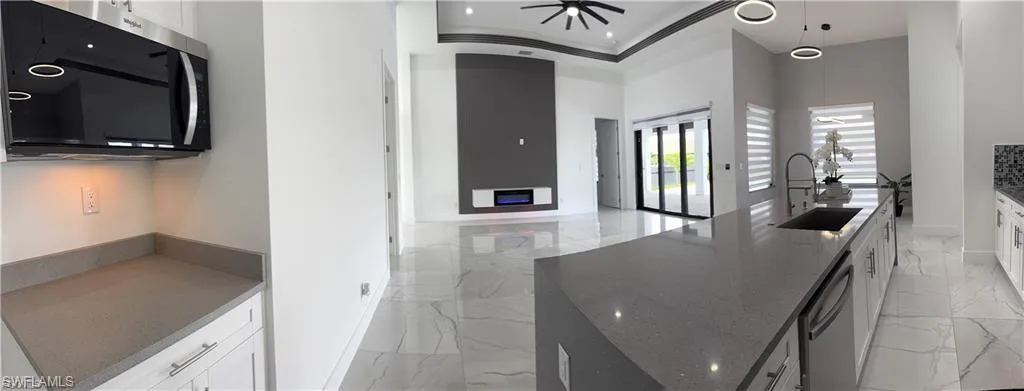 Kitchen featuring dark stone counters, stainless steel appliances, white cabinetry, light marble finish flooring, and ceiling fan