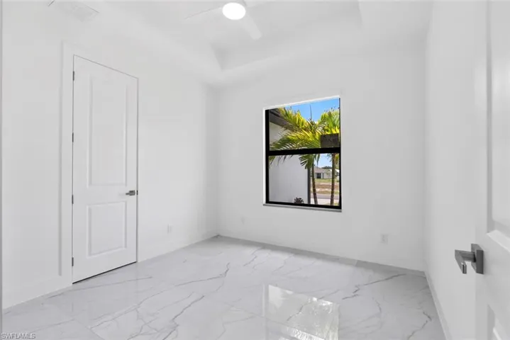 Empty room featuring a tray ceiling, light marble finish floors, and ceiling fan