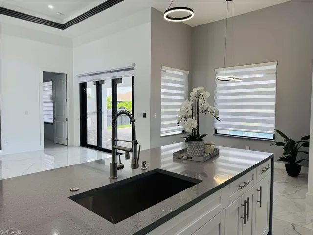 Kitchen featuring light marble finish flooring, dark stone countertops, pendant lighting, and white cabinets