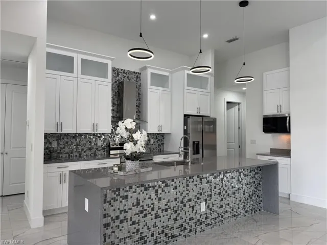 Kitchen featuring light marble finish floors, dark stone countertops, wall chimney range hood, stainless steel appliances, and white cabinetry