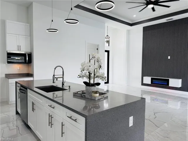Kitchen featuring light marble finish floors, white cabinetry, dark stone countertops, decorative light fixtures, and an island with sink