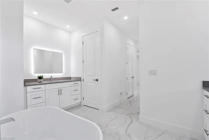 Bathroom with vanity, a soaking tub, light marble finish floors, and recessed lighting