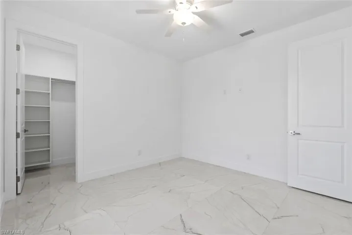 Unfurnished bedroom with light marble finish flooring, a spacious closet, and ceiling fan