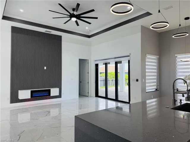 Living room featuring a raised ceiling, a glass covered fireplace, and ceiling fan