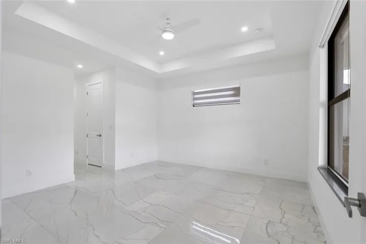 Unfurnished room featuring plenty of natural light, a tray ceiling, light marble finish floors, and recessed lighting