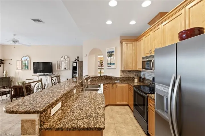Kitchen with kitchen peninsula, sink, appliances with stainless steel finishes, light brown cabinets, and dark stone counters