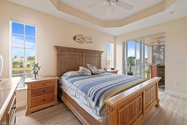 Bedroom with ceiling fan, light hardwood / wood-style floors, a raised ceiling, and access to outside