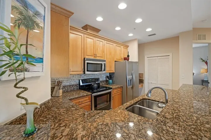 Kitchen with stainless steel appliances, decorative backsplash, light brown cabinetry, dark stone counters, and sink