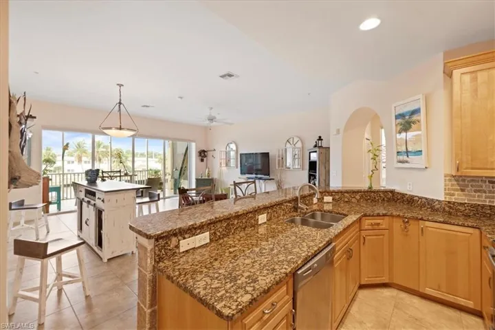 Kitchen with dark stone countertops, pendant lighting, stainless steel dishwasher, sink, and light tile patterned floors