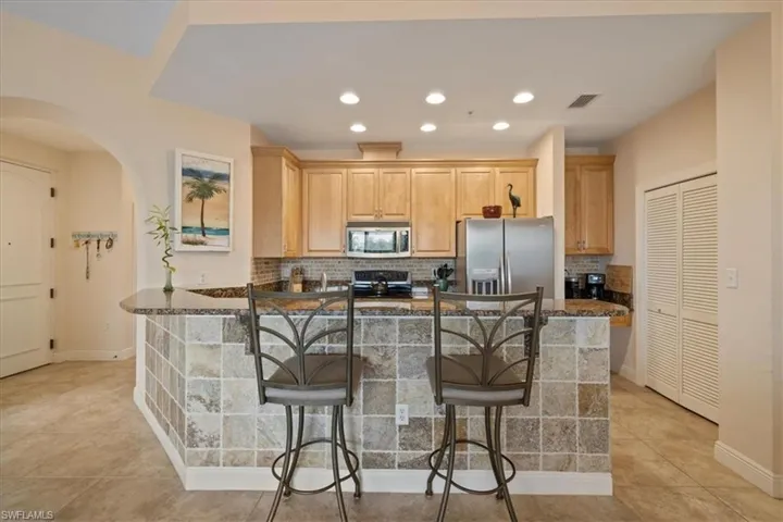 Kitchen with backsplash, appliances with stainless steel finishes, a breakfast bar area, light tile patterned floors, and light brown cabinetry
