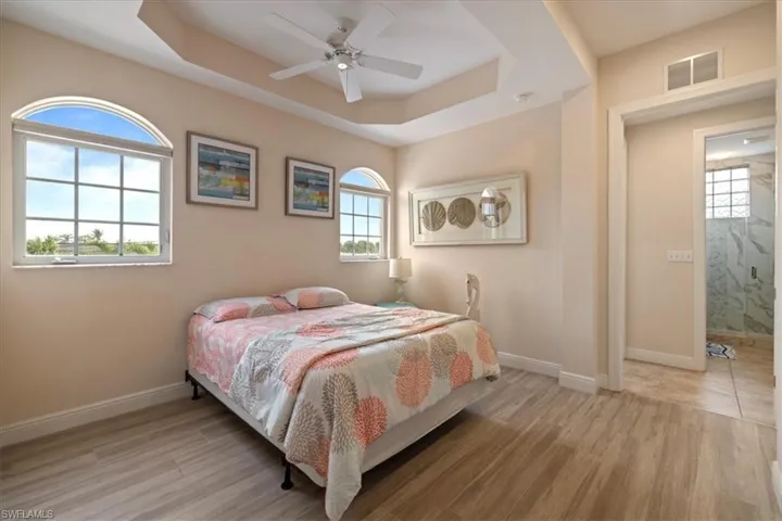 Bedroom with ceiling fan, ensuite bath, a tray ceiling, and light hardwood / wood-style flooring