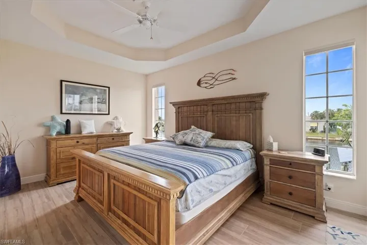 Bedroom with ceiling fan, a tray ceiling, and light wood-type flooring