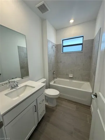 Full bathroom with vanity, tiled shower / bath, tile patterned flooring, and toilet